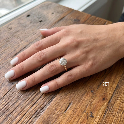 Shenae tulip solitaire ring worn on a hand resting on a wooden table