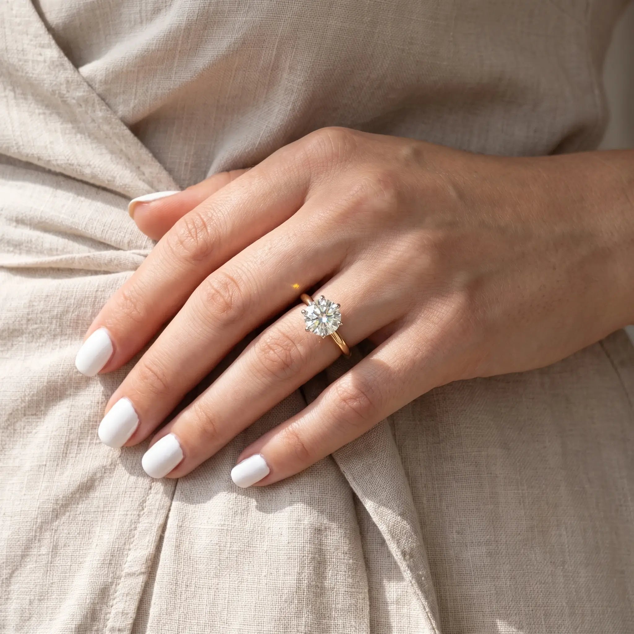 Hand with white nails wearing the Shenae tulip solitaire ring against a dress